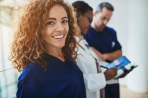 Smiling young female doctor standing in a hospital corridor with two medical colleagues talking in the background