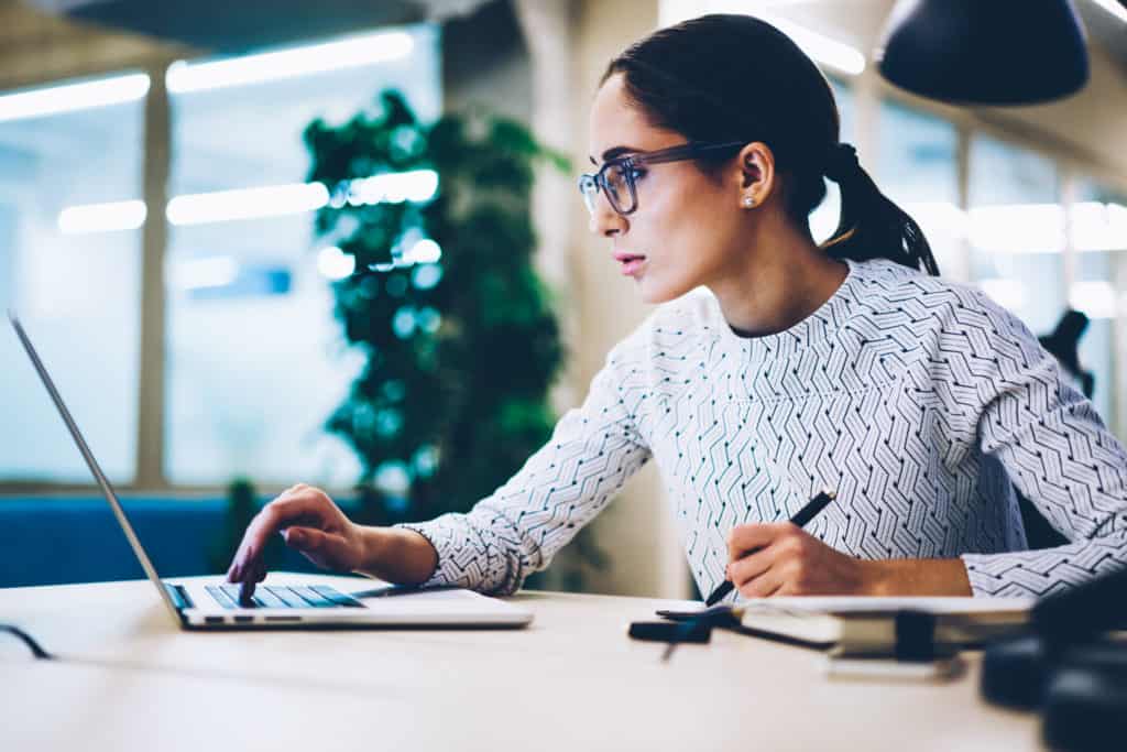 Serious female secretary reading information making booking on web page on laptop computer, businesswoman in eyewear for protect vision during working at netbook downloading files for financial report