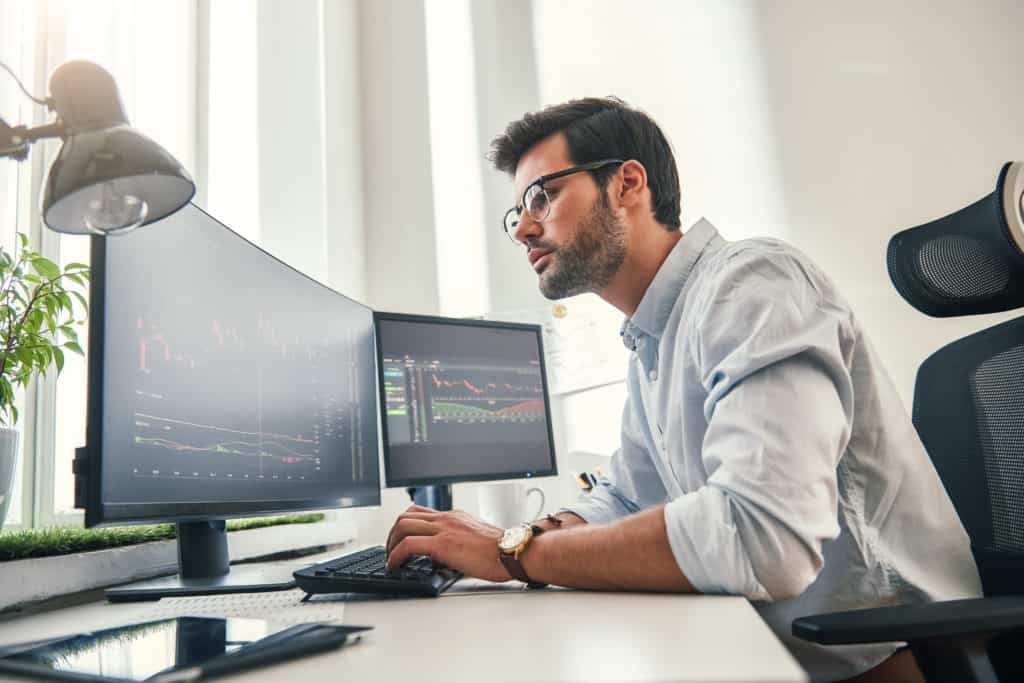 Confident businessman. Young bearded trader in formal wear is analyzing trading charts on computer screens while sitting in his modern office. Stock exchange. Trade concept. Investment concept
