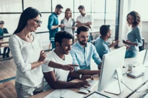 Young Smiling Business People Working in Office. Group of Young Coworkers Sitting Together at Table and Working on Laptops in Modern Office. Teamwork Concept. Corporate Lifestyle