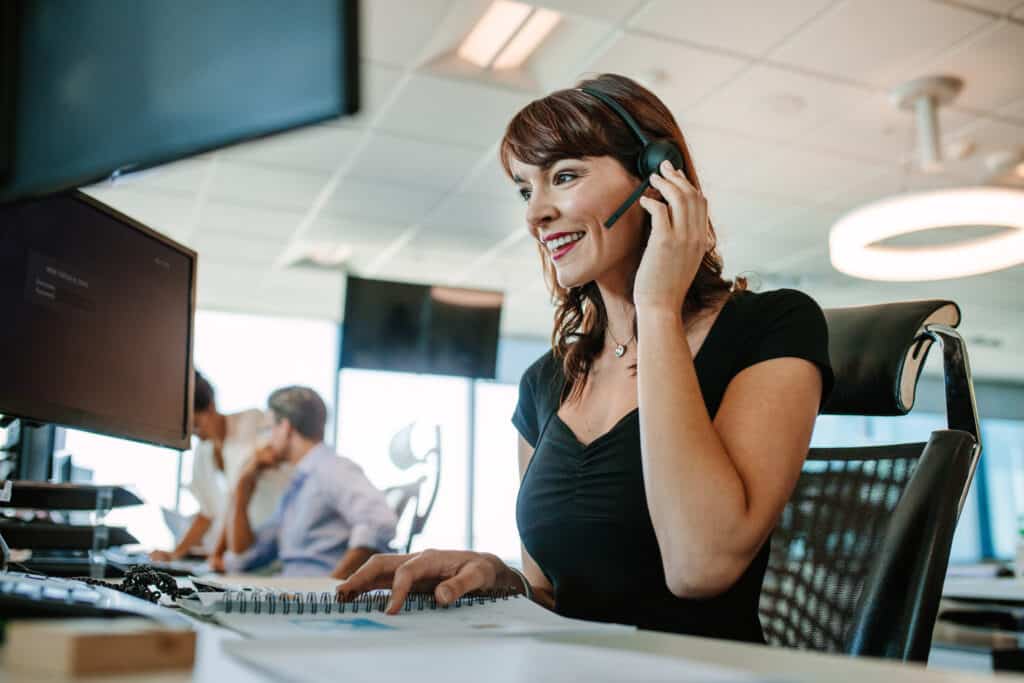 Woman smiles answering the phone on a headset in a call center setting